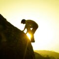 Como crescer mesmo quando tudo parece desmoronar Homem subindo uma montanha ao pôr do sol simbolizando superação e força mental